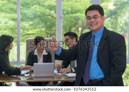 Smile middle aged businessman holding Thumbs up and standing. Confident senior businessman with group of business people meeting.