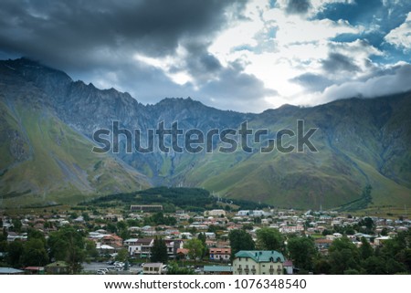 Beautiful landscape of majestic mountains, dramatic clouds and sky. View from the hill on village in the green valley