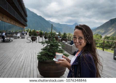 Young happy woman stands on the terrace of the hotel with cup of coffee in the morning. Handsome girl in good mood and is ready for adventures.