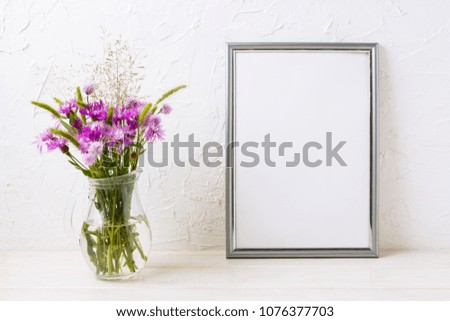 Silver frame mockup with purple burdock flowers in the glass jug. Empty frame mock up for presentation artwork. Template framing for modern art.