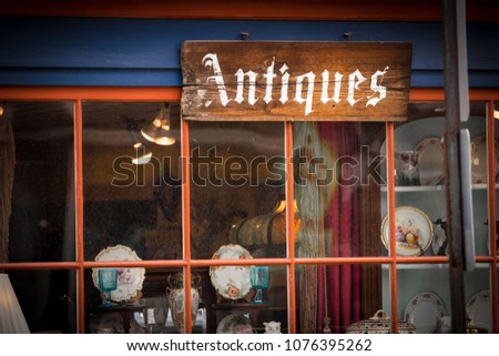 Wooden antiques sign on window of old antique shop; dishes and china on display.