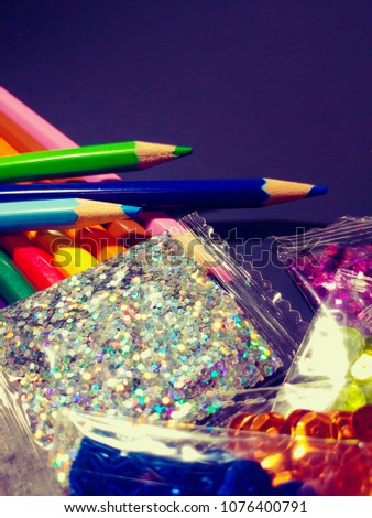 Pile of Craft Supplies With Copy Space. Color Pencils, Bags of sequins isolated on blue backdrop.