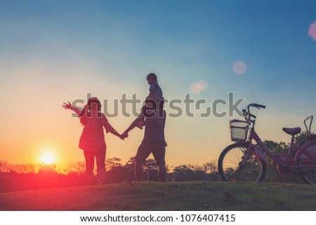 Happy family together, parents with their little child at sunset. Father raising baby up in the airing the sky on a holiday on Chatuchak Park at Bangkok City, Thailand. Concept of friendly family.