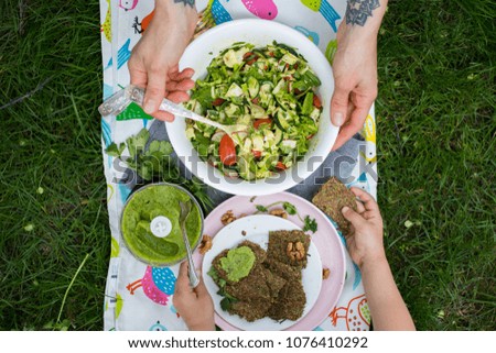 Woman hands and little girl hands holding vegetable salad with spinach, cabbage, cucumbers, tomatoes, olive oil on picnic. With avocado dip and flax flatbreads. Raw vegan vegetarian healthy food