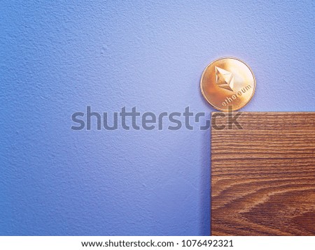 The Ethereum crypto currency coin is on a wooden board against a blue concrete wall. Image on the topic of earnings in the Internet and in the real world