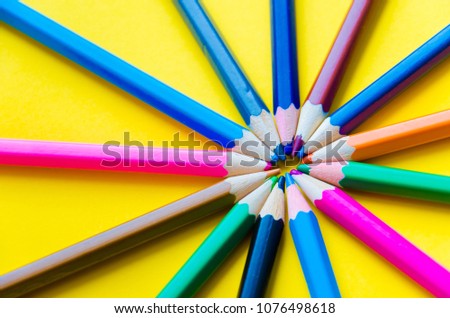 Color pencils in arrange in color wheel colors on yellow background