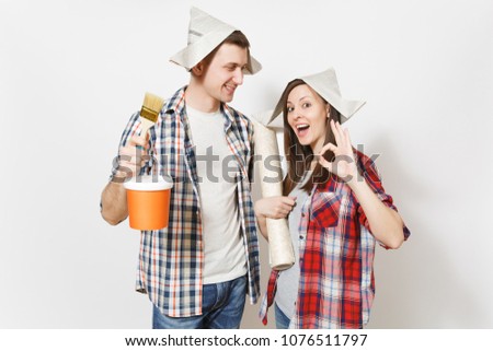 Young happy woman, man in casual clothes holding paint brush, paint bucket and wallpaper roll. Couple isolated on white background. Instruments for renovation apartment room. Repair home concept