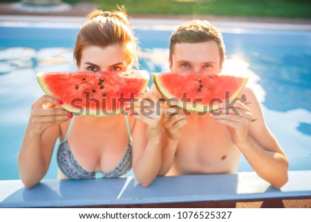 young beautiful couple in pool eating watermelon at sunset