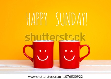 Two red coffee mugs with a smiling faces on a yellow background with the phrase Happy sunday. Happy coffee mugs. Royalty-Free Stock Photo #1076530922