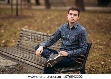 Nice guy sitting on the bench outdoors in cloudy weather