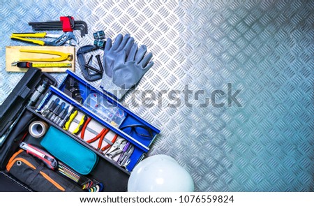 Top view of tools box and helmet on checkered plate background in workshop. Service tools set. Home building and electrical tools. Plumber hand tools. Technician equipment for repair work.