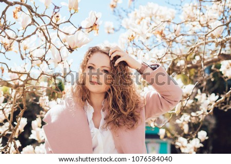 curly young woman posing in a park on a background of fragrant magnolia, enjoying spring and sun