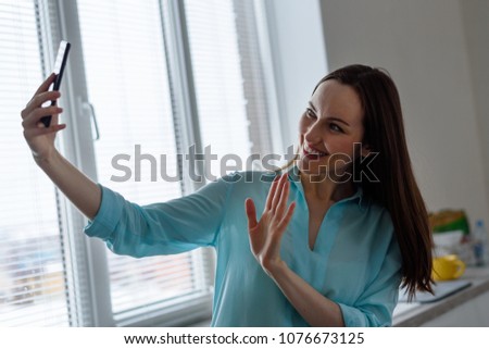 young girl takes a selfie on the front camera in the interior of the kitchen at home, welcomes open hand