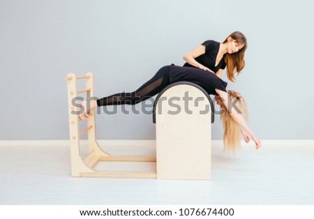 Young blond girl doing swan pilates exercises on ladder barrel with attractive female instructor in modern pilates studio.