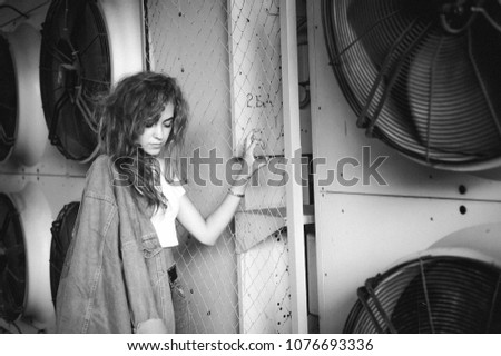 street portrait of a young attractive emotional girl with curly hair dressed in a trendy denim suit on the style. against the background of air conditioner ventilator systems.