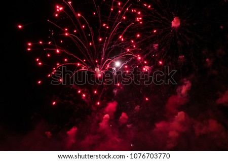 Fireworks with trails and smoke in red color against a black sky as background.