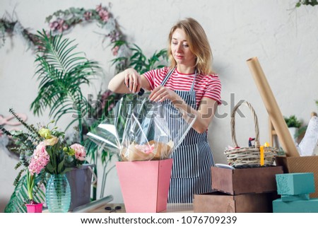 Picture of florist woman with stapler decorating flower arrangement at table with flowers, boxes