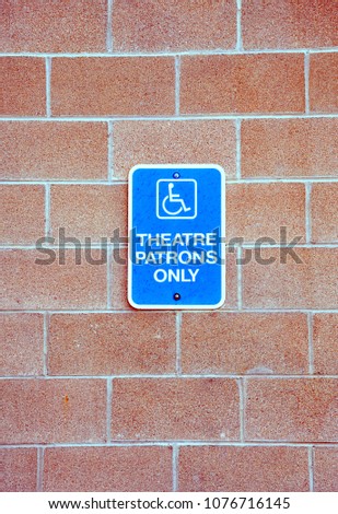 Theatre patrons disable parking sign posted outside on a brick wall.