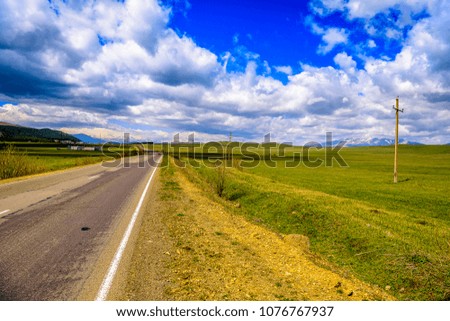 Beautiful road trip photo of empty road against blue skies, puffy clouds, rolling mountains and hills. 
