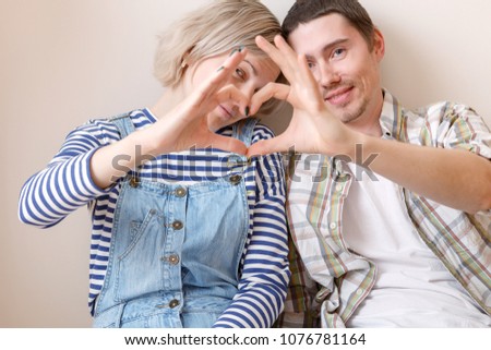 Photo of young married couple with heart from palms sitting on floor among cardboard boxes