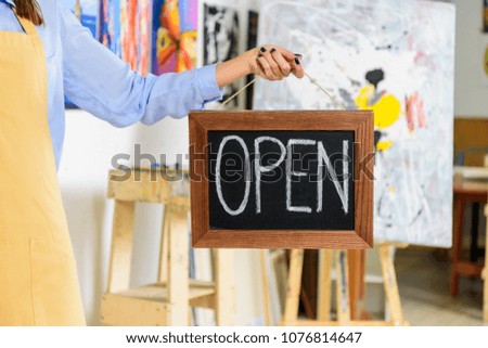 cropped image of female artist holding signboard with word open in workshop
