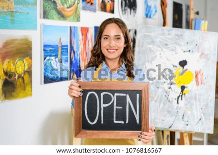 smiling beautiful female artist holding signboard with word open in workshop