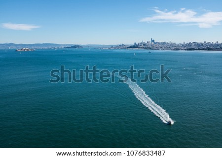 Speedboat cutting trhough the water of San Francisco bay below golden gate bridge on a sunny clear bright summer day with skyline cityscape of town in background

