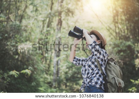 Woman with binoculars and telescope in rain forest. Hiking concept.