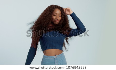 Beauty mixed race african american woman with hair blowed in air smiling at camera dancing on blue background