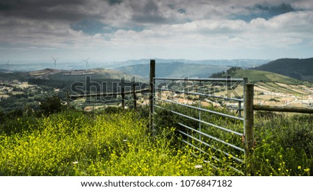 A fence sits on top of some grass with a hilly landscape in the background.