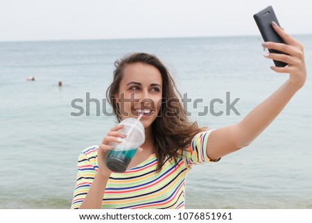 Beach woman drinking cold drink beverage having fun at beach party. Female babe in bikini enjoying Ice tea, coke or alcoholic drink smiling happy. holding a smartphone device taking selfies pictures
