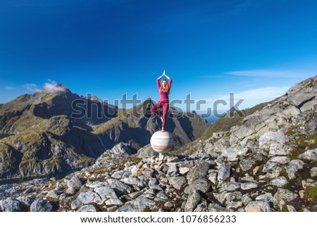 The blond hair girl is standing in yoga position asana vrikshasana on stone sphere - Jupiter monument in mountains on Munkan mountain on the Lofoten Islands beyond the Arctic circle in Nordic Norway