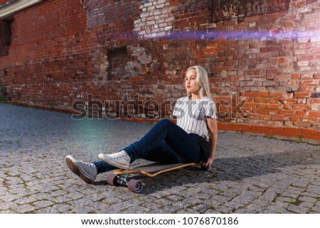 Beautiful young blonde girl riding longboard in sunny weather