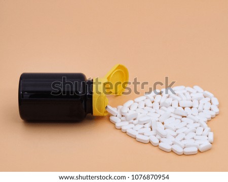 Pills spilling in heart shaped out from pill bottle     and isolated on light brown background. For medical and healthcare concept with copy space.