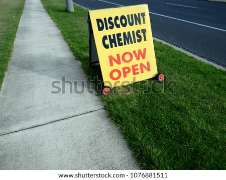 yellow sign on the side of the road on the cement footpath, discount chemist, now open.