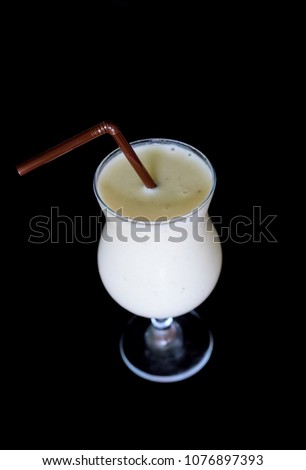 White cocktail on dark background. Milk smoothie in glass with straw. Milkshake top view isolated. Cafe or restaurant menu picture. Creamy smoothie with vanilla or tropical fruit. Children milk drink