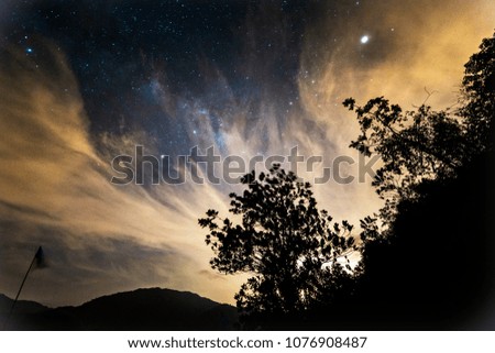 Starry landscape, milkyway scene over trees and alps, covered by clouds during night. (Visible noise, motion blur and soft focus due to high ISO, long exposure and shallow DOF).