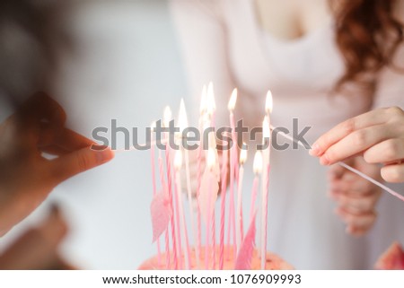 
girls light candles on a cake. 
Girls in pink dresses light candles from candles on a birthday cake