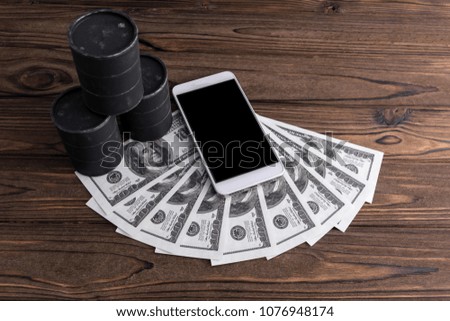 barrels of oil, dollars, a smartphone with a black screen on a wooden background. sale rate