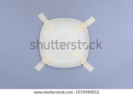 White plate, dish fixed with an adhesive tape on a gray background. Concept of storage, feeling safe, protect, relocation