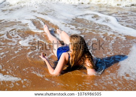 Girl in a blue bathing suit lies on the seashore and relaxes. Waves caress the girl's body.