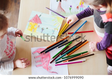 Little girls drawing a colorful pictures of elephant and playing children using pencil crayons standing at table indoors. Shot from above