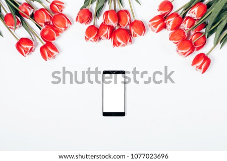 Mobile phone with blank screen and bouquets of red tulips on a white table top view