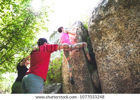 Climbing in nature. Friends climb to the stone. The girl climbs on the stone, and friends support her. Bouldering in nature. Active lifestyle. Sports people. Gymnastic insurance.
