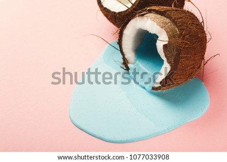 Blue paint flowing from coconut half on pink table. Creative background with copy space, bold design for poster or clothing print