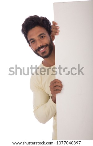 Handsome young man wearing a t-shirt, standing behind a billboard, on his face big smile, isolated on white background