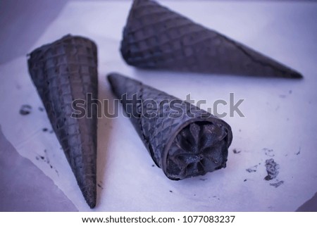 Trendy food. Black ice cream in traditional  black cones on white paper. Soft focus.