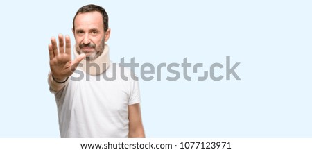 Injured senior man using a neck brace annoyed with bad attitude making stop sign with hand, saying no, expressing security, defense or restriction, maybe pushing isolated over blue background