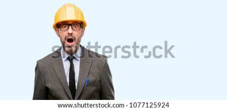 Senior architect or engineer scared in shock, expressing panic and fear isolated over blue background