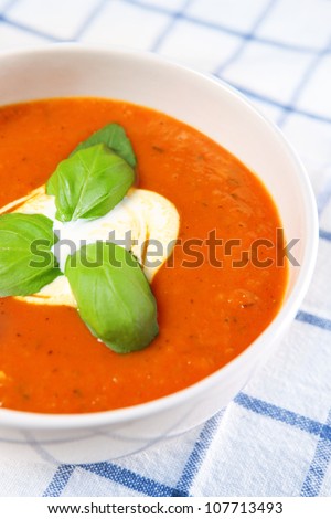 A picture of a white bowl full of fresh tomato soup with basil leaves on top